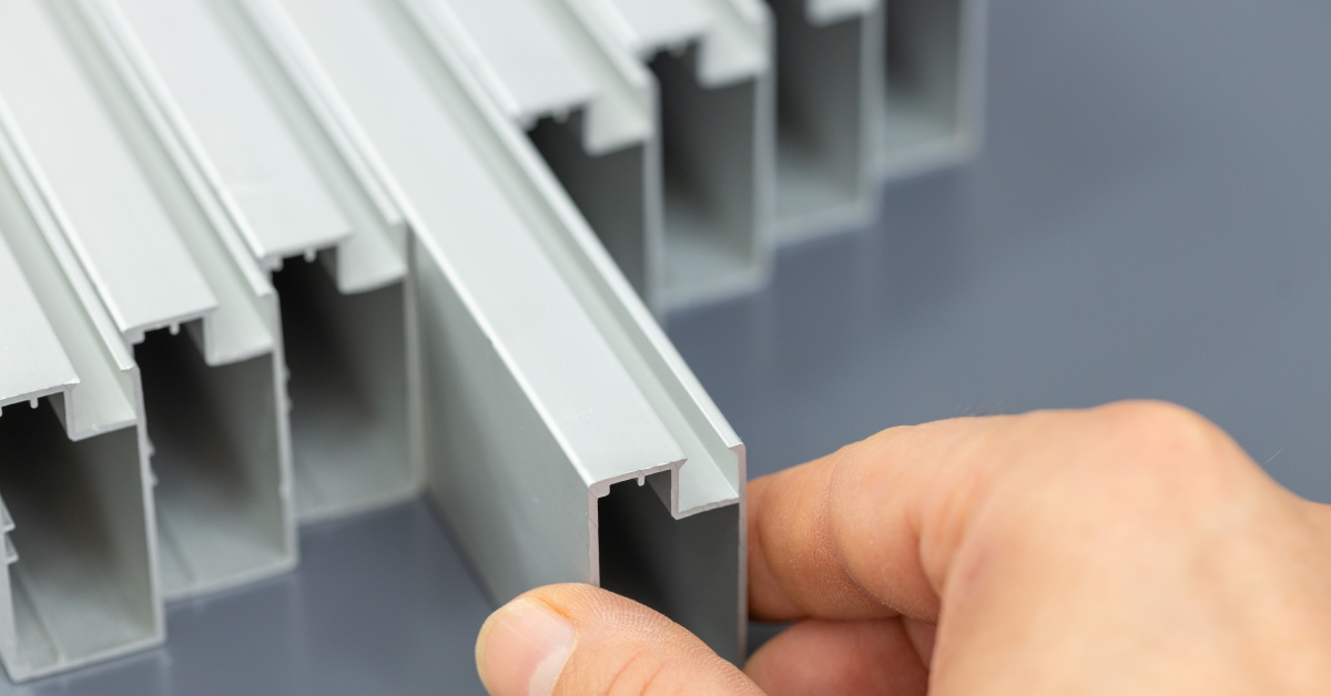 A collection of aluminum profiles on a gray background with a hand holding them, highlighting its use in construction.