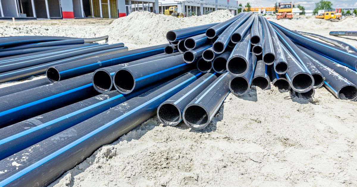 A scattered stack of plastic tubing at a construction site. They are black with a blue stripe down the pipe.