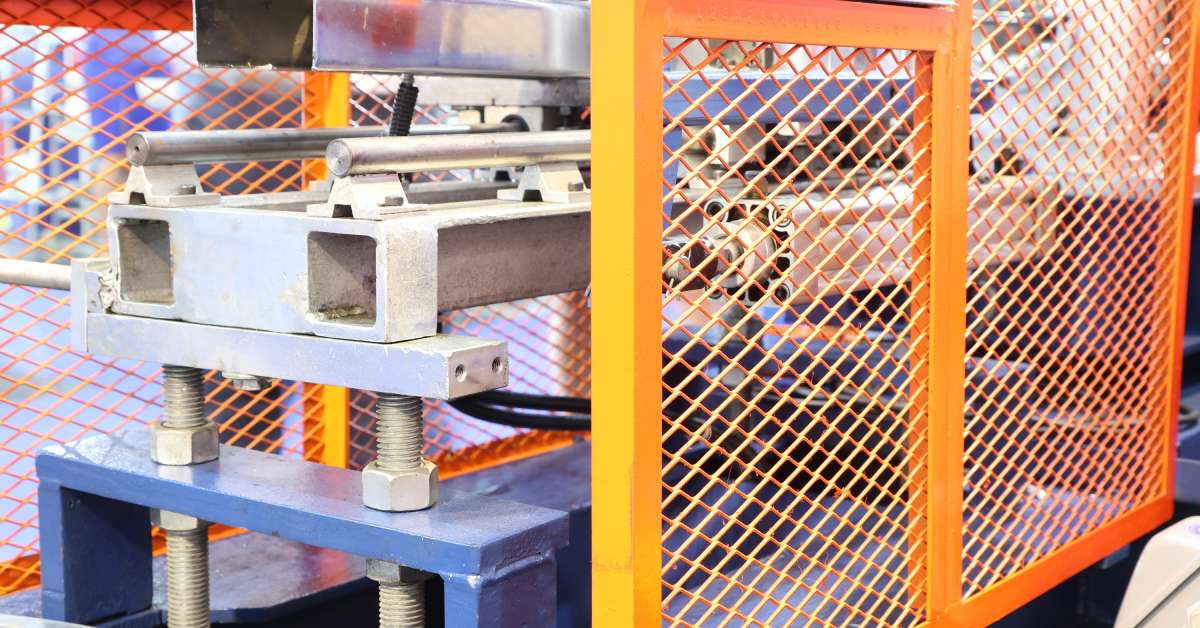 An orange machine guard protecting machine equipment. The guard is made of sturdy aluminum with a lattice design.