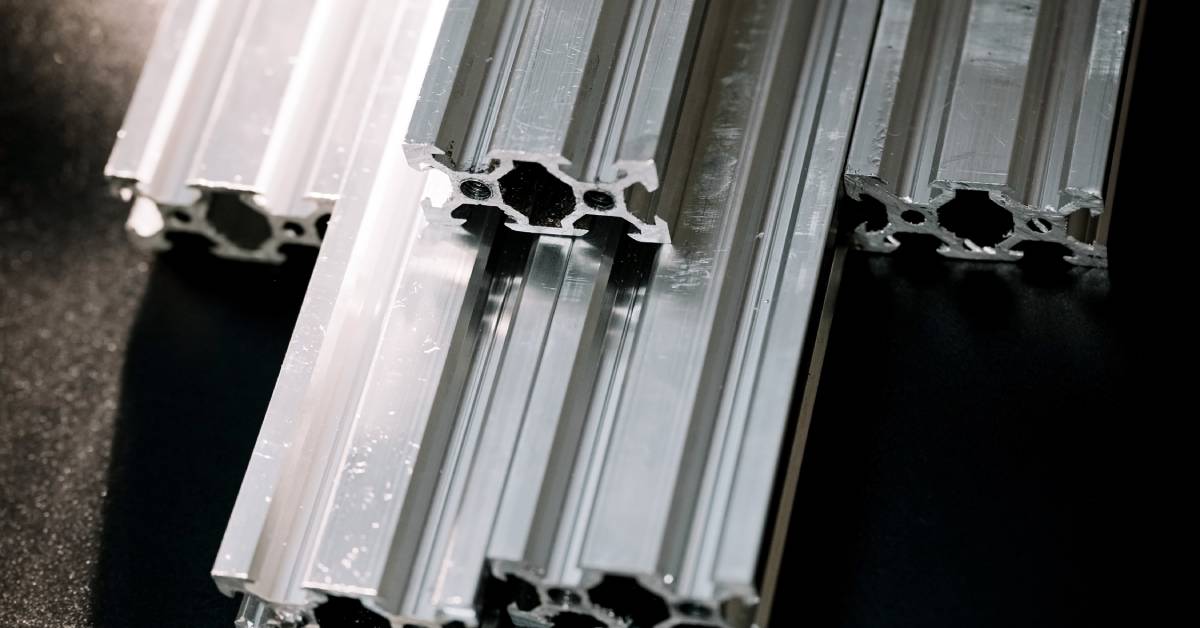 Aluminum extrusion profiles stacked on a black surface. There are ten extrusions in total with the same profile.