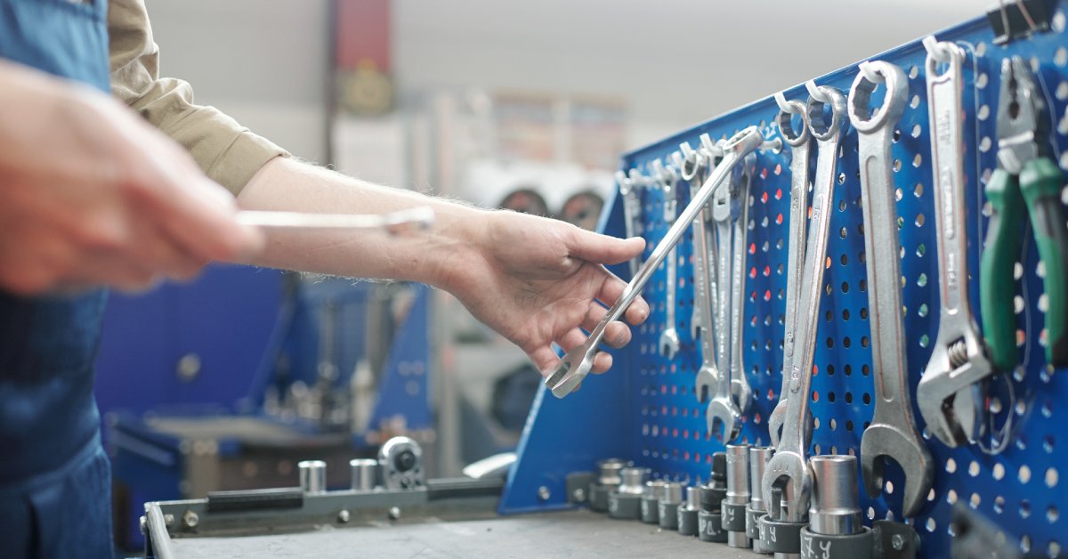 A workbench with a variety of tools hanging on a peg board. There is a hand reaching for a wrench on the workbench.